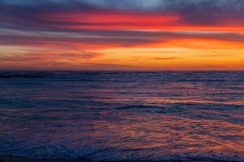 Dramatic Golden sunset over tranquil beach, waves lashing the pebble coastlin Stock Photos