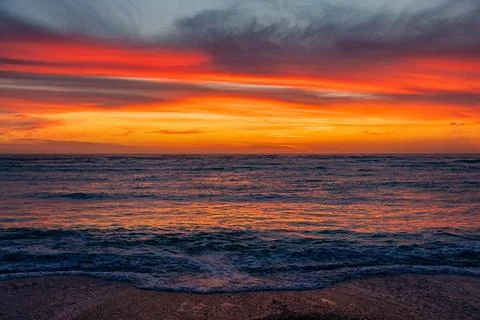 Dramatic Golden sunset over tranquil beach, waves lashing the pebble coastlin Stock Photos