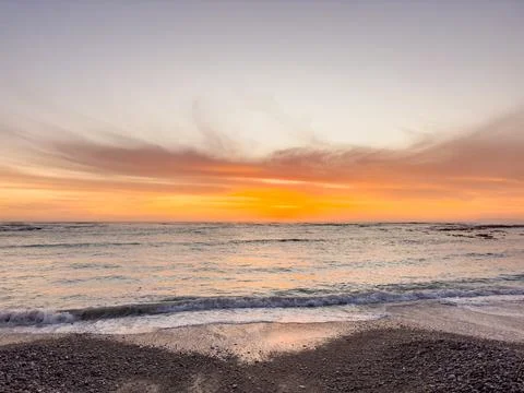 Dramatic Golden sunset over tranquil beach, waves lashing the pebble coastlin Stock Photos