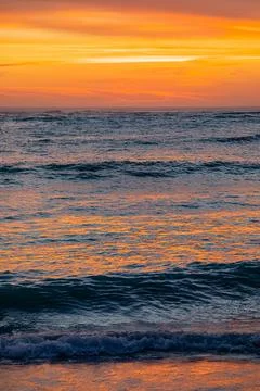 Dramatic Golden sunset over tranquil beach, waves lashing the pebble coastlin Stock Photos