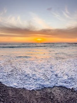 Dramatic Golden sunset over tranquil beach, waves lashing the pebble coastlin Stock Photos