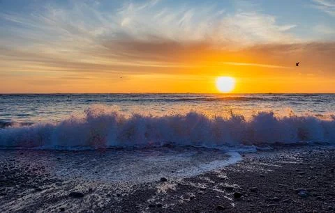 Dramatic Golden sunset over tranquil beach, waves lashing the pebble coastlin Stock Photos