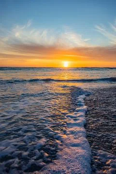 Dramatic Golden sunset over tranquil beach, waves lashing the pebble coastlin Stock Photos
