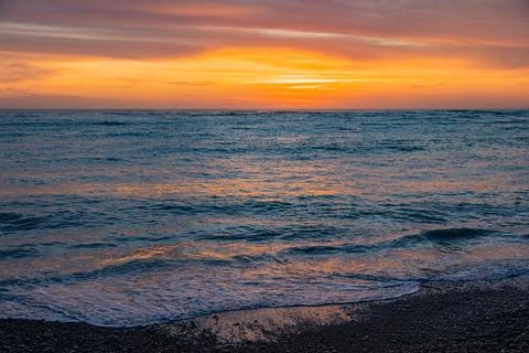 Dramatic Golden sunset over tranquil beach, waves lashing the pebble coastlin Stock Photos