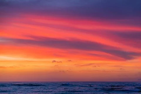 Dramatic Golden sunset over tranquil beach, waves lashing the pebble coastlin Stock Photos