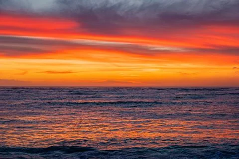 Dramatic Golden sunset over tranquil beach, waves lashing the pebble coastlin Stock Photos