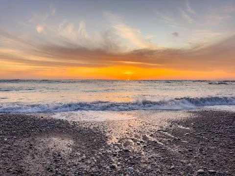 Dramatic Golden sunset over tranquil beach, waves lashing the pebble coastlin Stock Photos