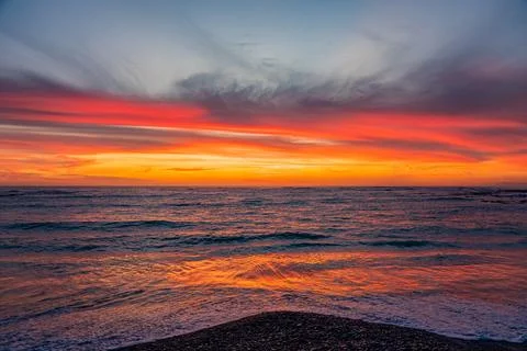 Dramatic Golden sunset over tranquil beach, waves lashing the pebble coastlin Stock Photos