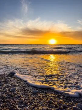 Dramatic Golden sunset over tranquil beach, waves lashing the pebble coastlin Stock Photos