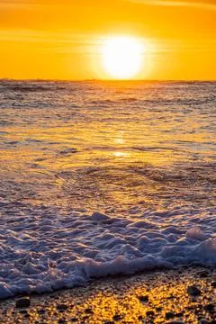 Dramatic Golden sunset over tranquil beach, waves lashing the pebble coastlin Stock Photos