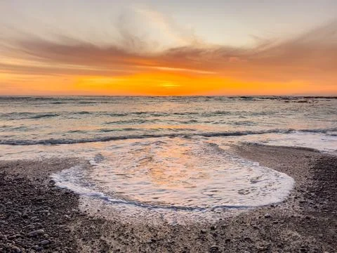 Dramatic Golden sunset over tranquil beach, waves lashing the pebble coastlin Stock Photos