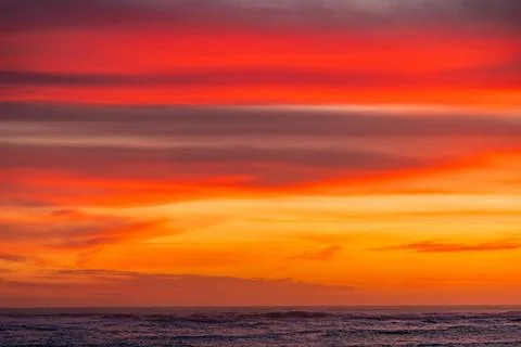 Dramatic Golden sunset over tranquil beach, waves lashing the pebble coastlin Stock Photos