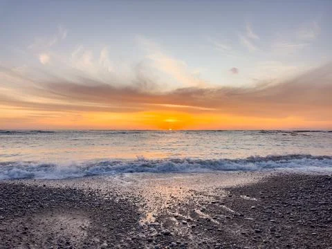 Dramatic Golden sunset over tranquil beach, waves lashing the pebble coastlin Stock Photos