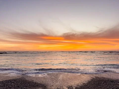 Dramatic Golden sunset over tranquil beach, waves lashing the pebble coastlin Stock Photos