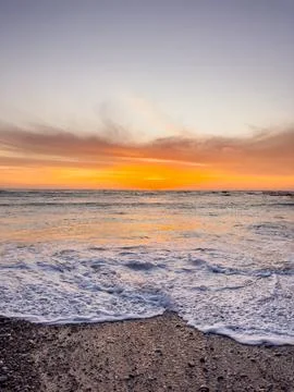 Dramatic Golden sunset over tranquil beach, waves lashing the pebble coastlin Stock Photos