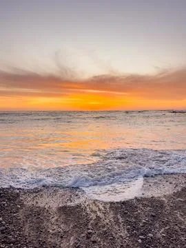 Dramatic Golden sunset over tranquil beach, waves lashing the pebble coastlin Stock Photos