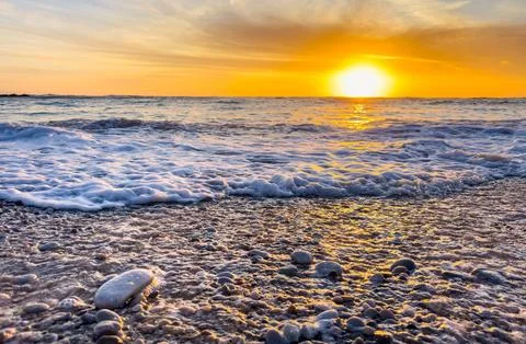 Dramatic Golden sunset over tranquil beach, waves lashing the pebble coastlin Stock Photos