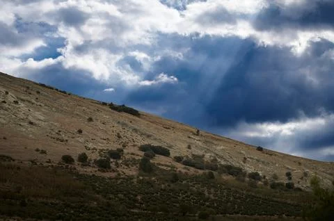 Dramatic hillside landscape with sun rays breaking through storm clouds Stock Photos