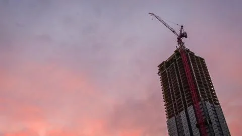 Dramatic Horizontal residential tower with construction crane against orange sky Stock Photos