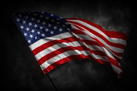 A dramatic image of the American flag waving against a dark cloudy background Stock Photos