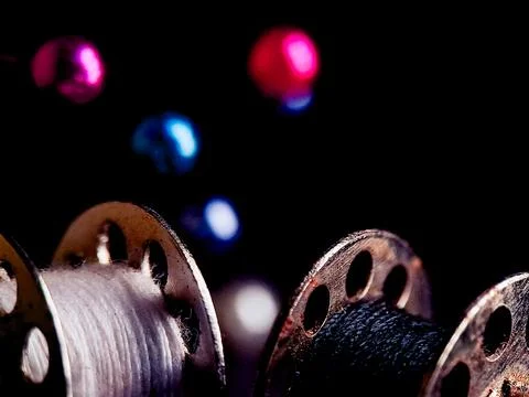 Dramatic image featuring sewing bobbins and colorful sewing pins on a dark,.. Stock Photos