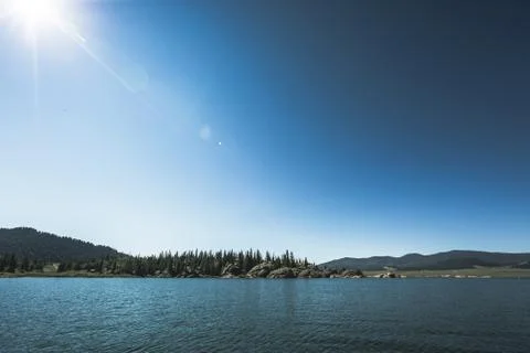 Dramatic lake and forest beneath mountain and blue sky Stock Photos