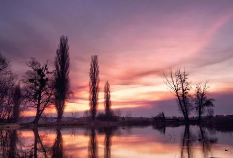 Dramatic landscape with beautiful glowing sky with clouds over a lake at suns Stock Photos