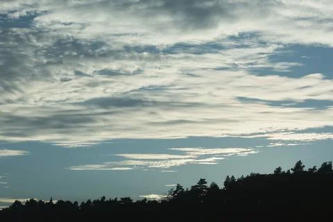 Dramatic layered clouds fill a wide blue sky above a silhouetted forested r.. Stock Photos