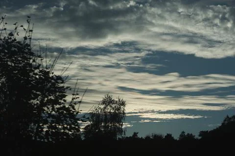 Dramatic layered clouds stretch across a moody twilight sky above dark silh.. Stock Photos