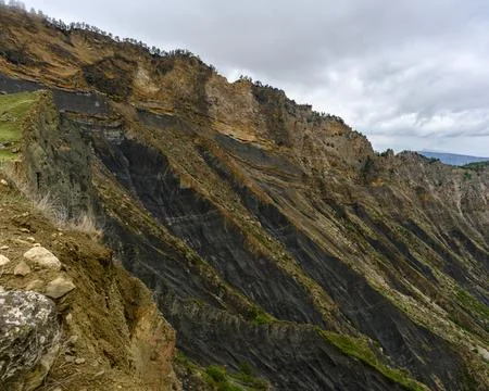 Dramatic layered rock formation on a mountain cliff under a cloudy sky 스톡 사진
