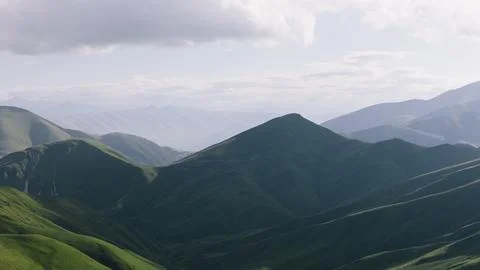 Dramatic light over rolling green mountain ridges under cloudy sky panorama Stock Photos