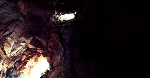 Dramatic light shines through rocky formations in deep cave Illustrazione stock