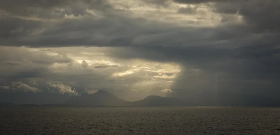 Dramatic light streams through storm clouds on the sea Stock Photos