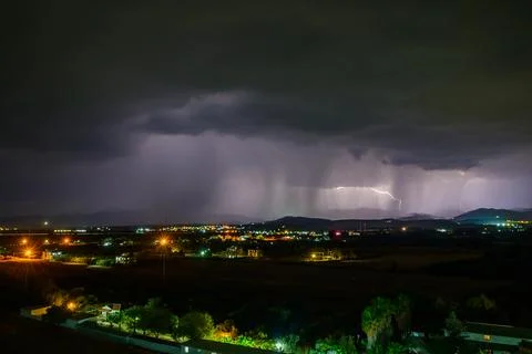 Dramatic lightning illuminates a stormy night over a sprawling cityscape. Stock Photos