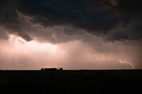 Dramatic lightning storm over rural farmhouse under dark thunderclouds and rain Stock Photos