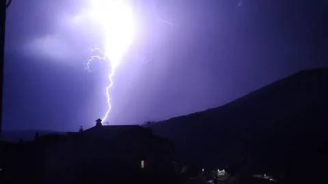 Dramatic lightning strike during a nighttime storm over a mountainous village Stock Photos