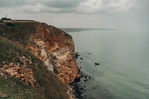 Dramatic limestone sea cliff above calm water under cloudy sky with wild gr.. Stock Photos
