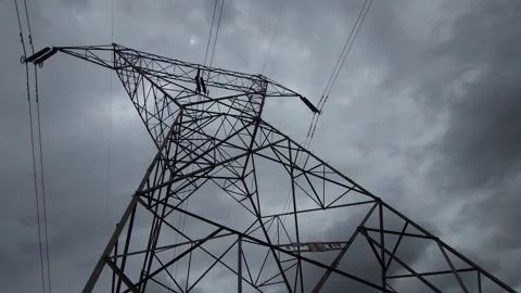 A dramatic, low-angle shot of a power pylon towering against dark overcast cloud Stockbeeldmateriaal 337476815