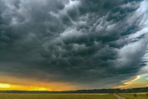 Dramatic mammatus storm clouds forming above a rural landscape during sunset Stock Photos