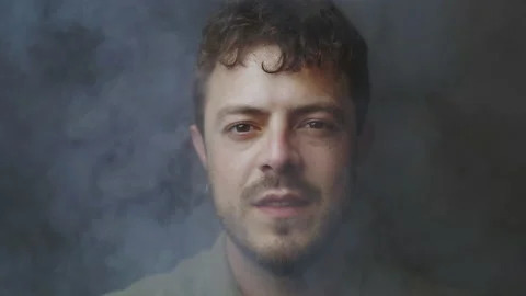 Dramatic man's face portrait looking in camera surrounded by fog and smoke Stock Footage 194047542