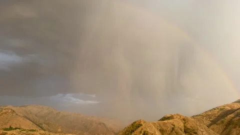 Dramatic mountain landscape with rain clouds and a vibrant rainbow arching over Stock Footage 345219373
