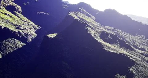 Dramatic mountain landscape with shadows and vibrant greenery at dawn Stock-Illustration