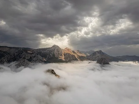 Dramatic mountain peaks rising above a sea of clouds under stormy sky Stock Photos
