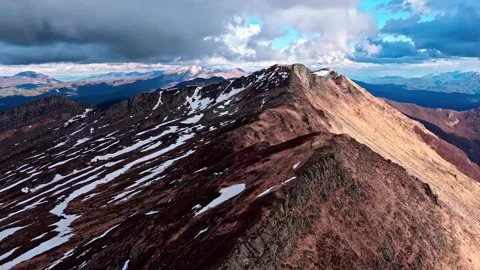 Dramatic mountain range aerial view with snow patches under cloudy sky. Stock Footage 341068517