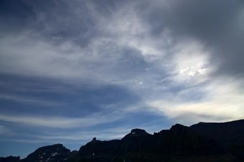 Dramatic Mountain Silhouettes Under Wispy Sky in Glacier National Park Stock Photos