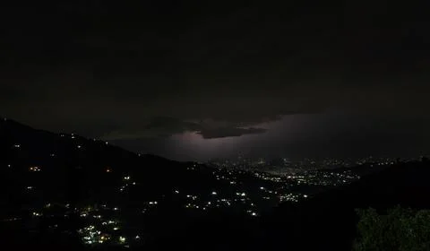 Dramatic night landscape over a mountainous town with glowing urban lights. 库存照片
