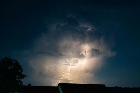 Dramatic nighttime lightning storm illuminating massive thundercloud. Stock Photos
