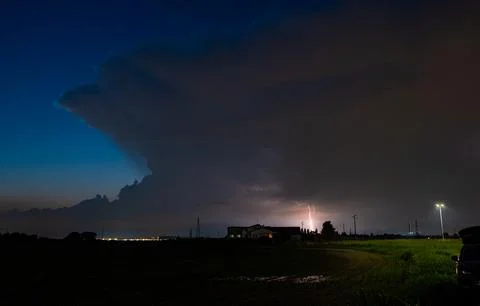 Dramatic nighttime thunderstorm with lightning bolt illuminating rural landscape Stock Photos