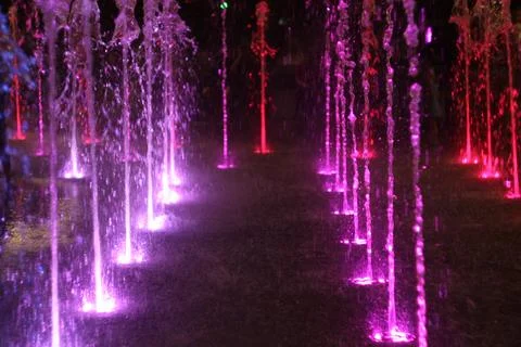 A dramatic nighttime view of a ground-level fountain with tall water streams lit Stock Photos