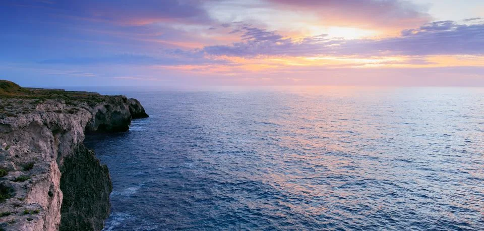 Dramatic ocean cliffs meet a pastel sky at sunset with gentle waves below Stock Photos
